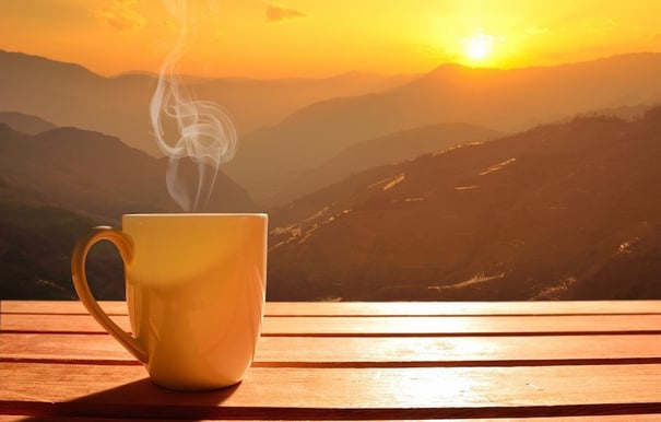 Cup of coffee with sunrise over mountains in the background.